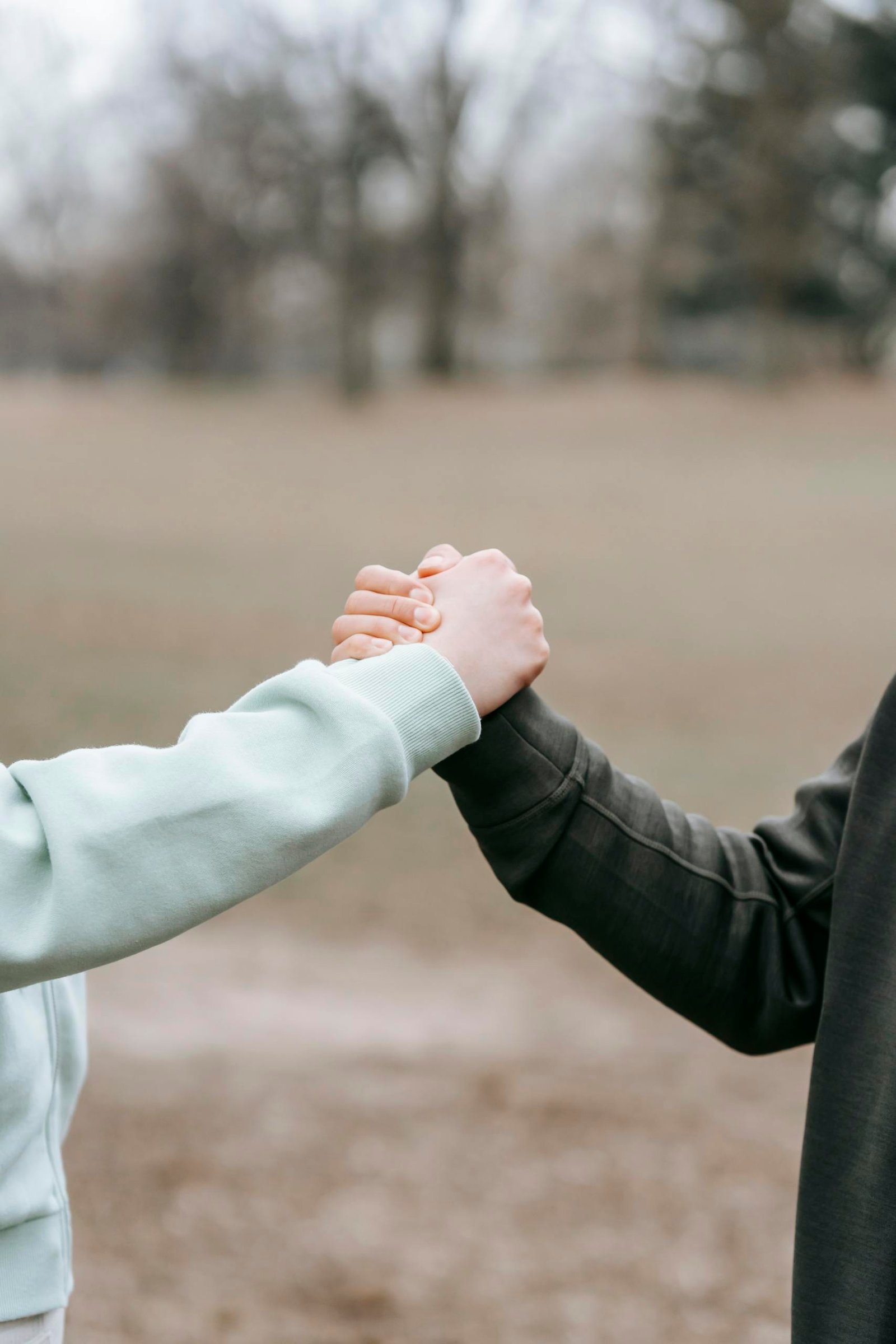 Two adults holding hands in an outdoor park setting, symbolizing trust and connection.