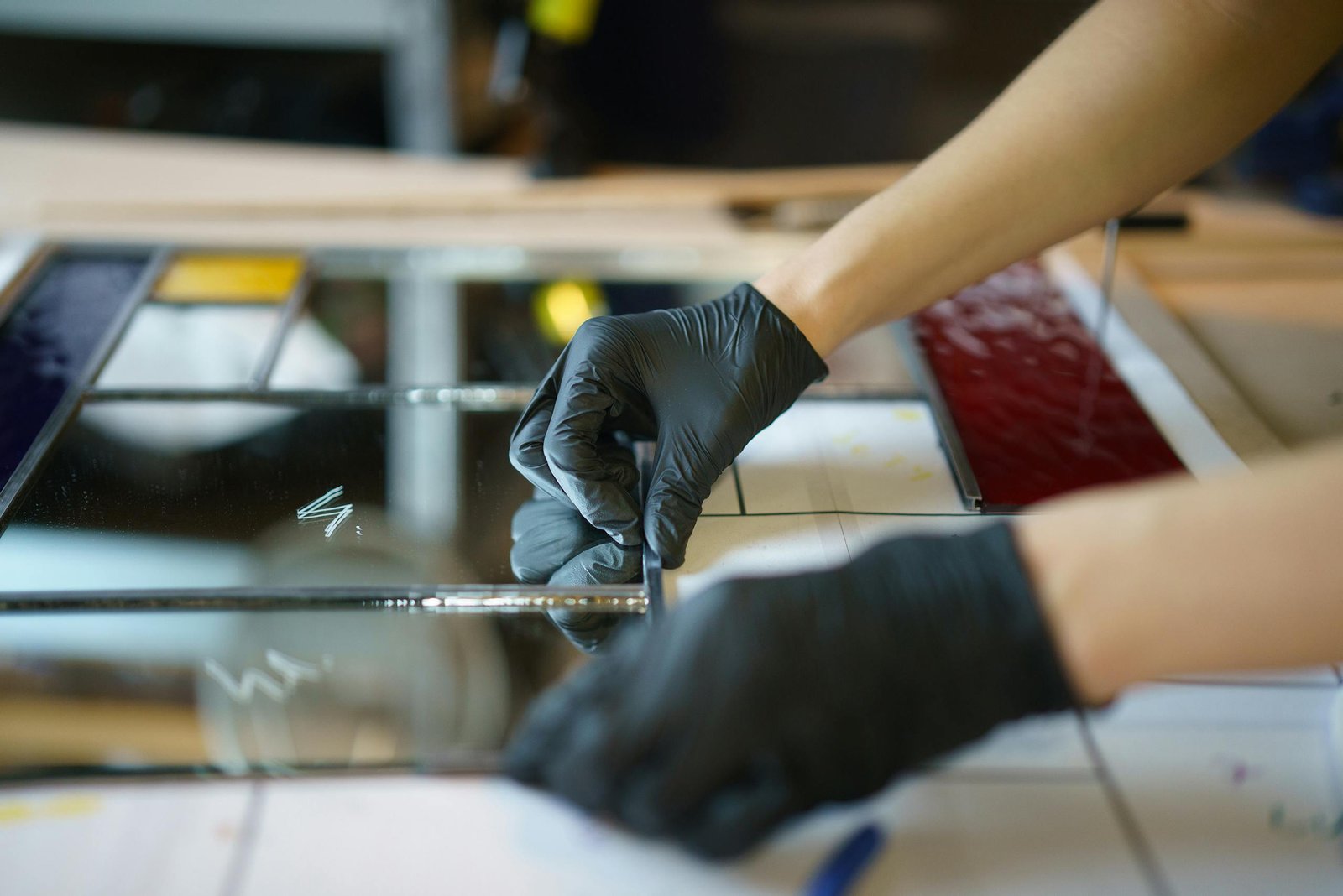 Detailed image of stained glass crafting with hands in rubber gloves assembling pieces.